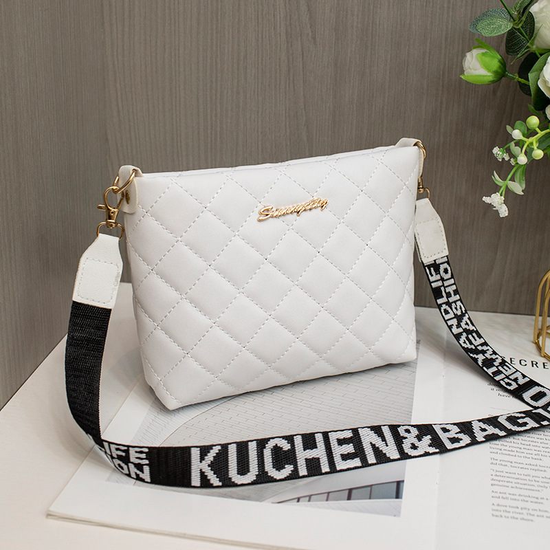 White quilted handbag with a black strap featuring 'Kuchen & Bag' on a wooden surface.