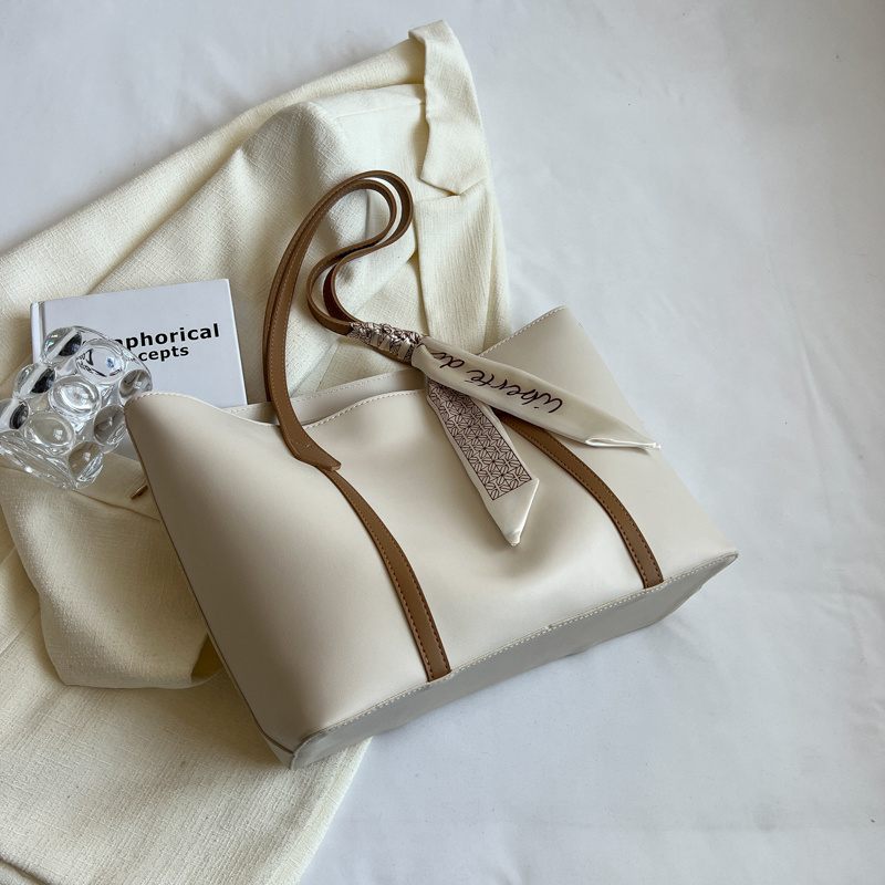 Beige handbag with brown handle and strap on a white surface
