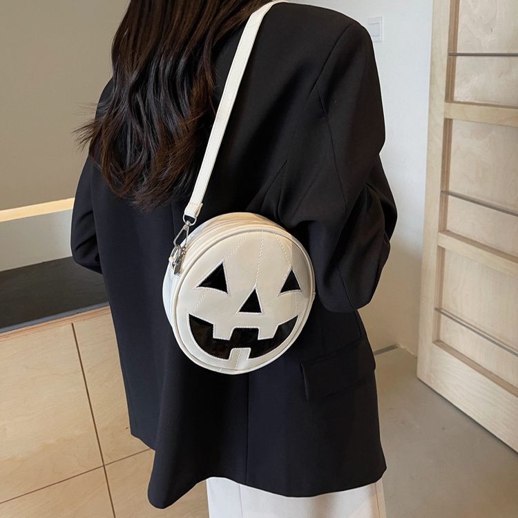 Person wearing a black outfit with a white round bag featuring a jack-o'-lantern face.