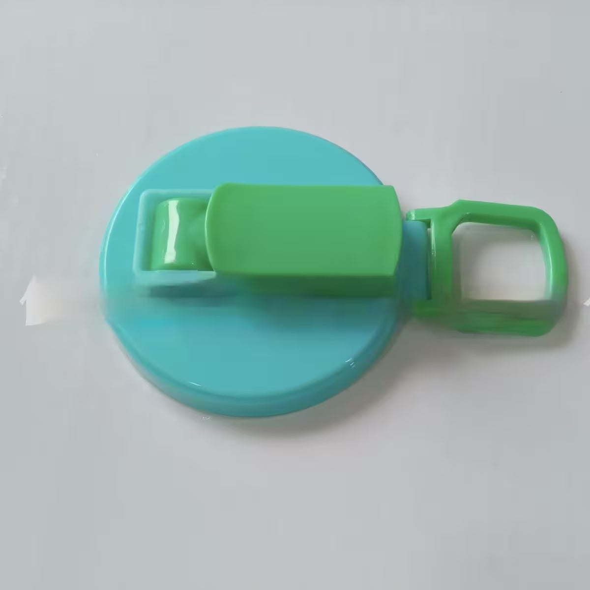 Turquoise and green plastic lid with a clip on a white background