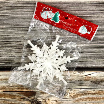 White snowflake decoration in clear packaging with a red 'Christmas Decorations' label on a wooden surface.