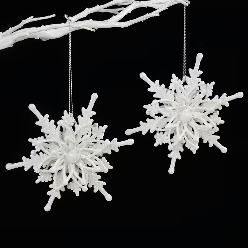 Two white snowflake-shaped ornaments hanging from a branch against a black background