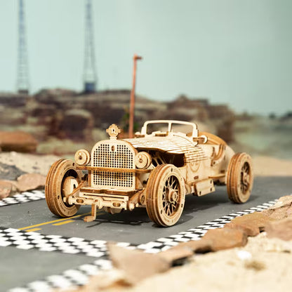 Wooden model of a vintage car on a miniature road with a blurred landscape in the background.