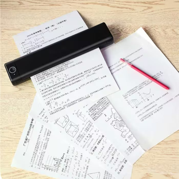 Black handheld scanner on top of printed documents with a red pen on a wooden surface