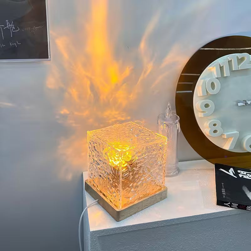 Decorative glass cube lamp on a shelf with a clock and other items in the background.