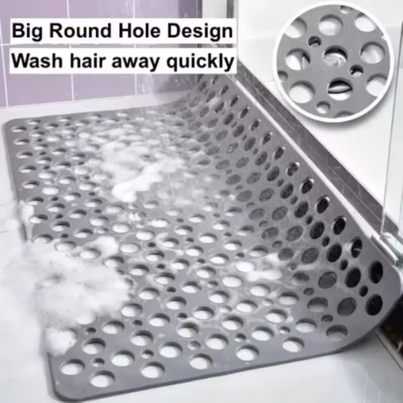 Gray bath mat with round holes on a bathroom floor, showing water and soap bubbles.