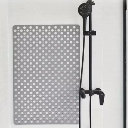 Gray polka dot shower mat with a black shower head on a white tiled wall background