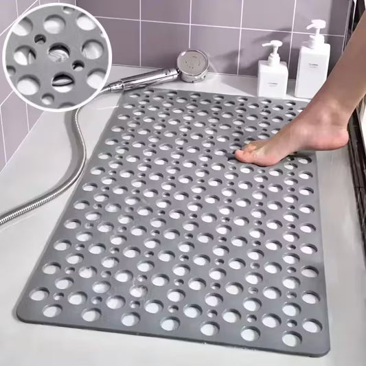 Gray perforated bath mat with a shower head and soap bottles on a tiled bathroom floor.