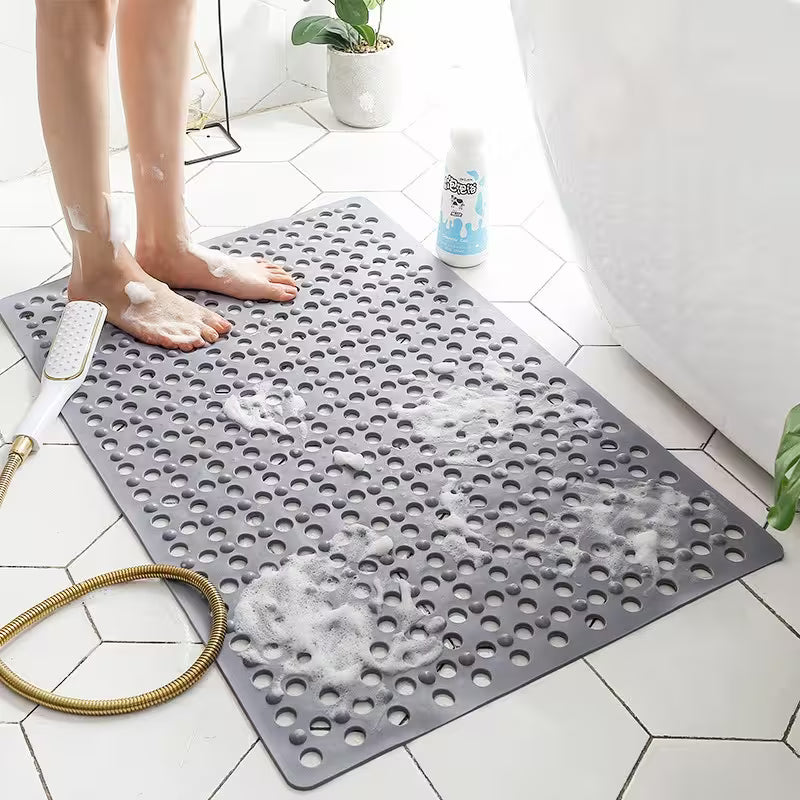Gray bath mat with holes on a bathroom floor, next to a bathtub and shower head.