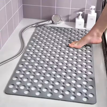 Gray perforated bath mat on a bathroom floor with a shower head and bottles in the background.
