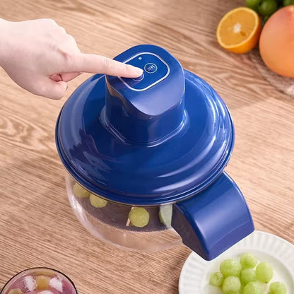 Blue juicer with a hand pressing a button, surrounded by fruits on a wooden table.