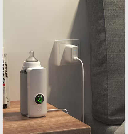 Baby bottle warmer plugged into a wall outlet on a wooden surface.