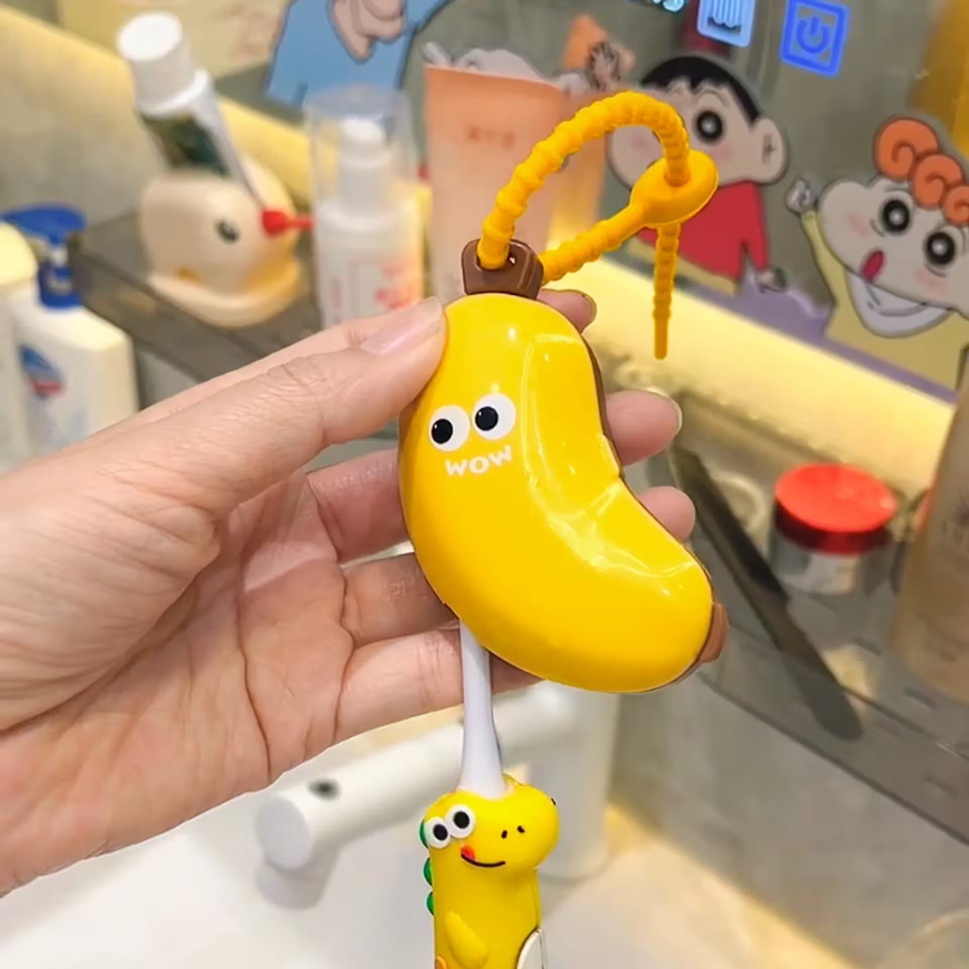 Hand holding a yellow banana-shaped toy with a face, against a background of cartoon characters.