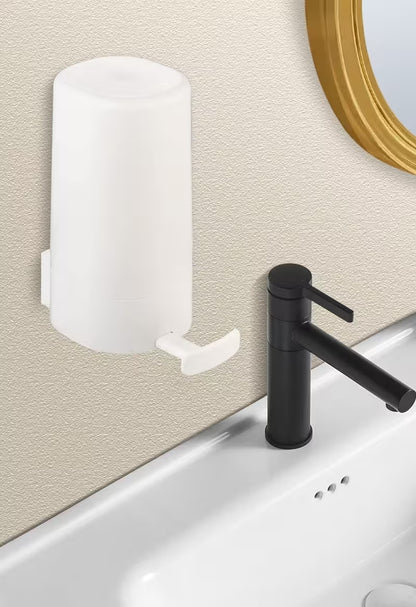 White soap dispenser attached to a beige wall above a sink with a black faucet.