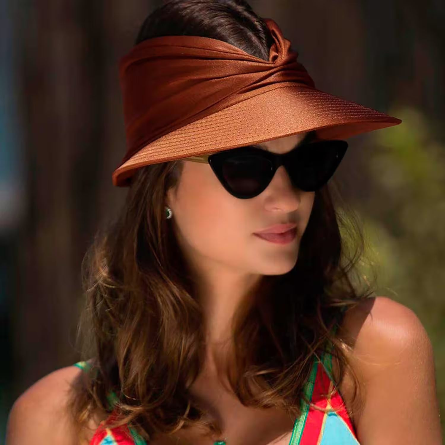 Woman wearing a brown visor hat and sunglasses with a blurred natural background