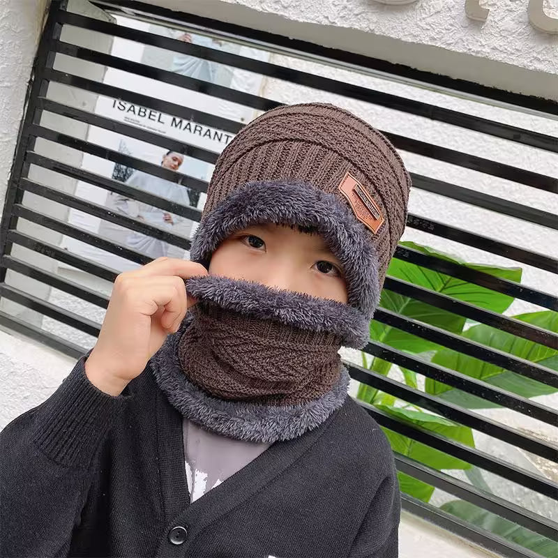 Child wearing a brown and gray knitted hat and scarf in front of a window with 'Isabel Marant' branding.