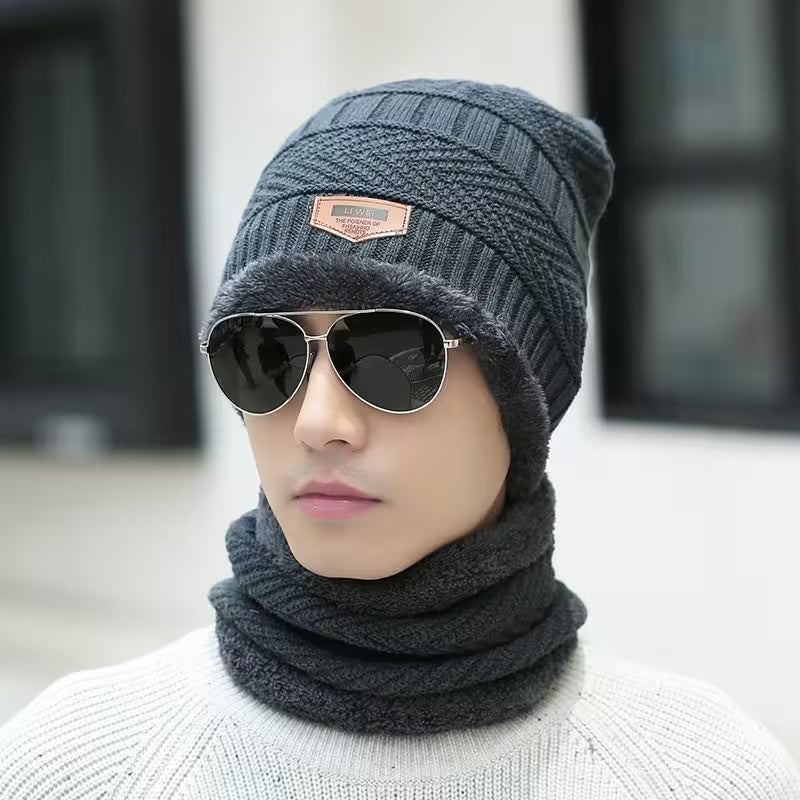 Mannequin wearing a gray knit beanie and scarf with sunglasses, against a blurred indoor background.