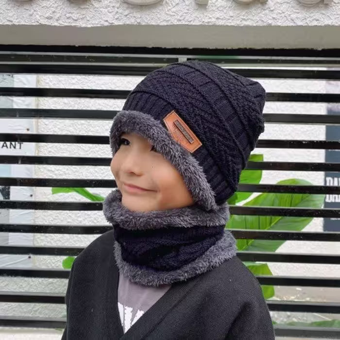 Child wearing a dark blue knit hat and gray scarf against a black metal fence background