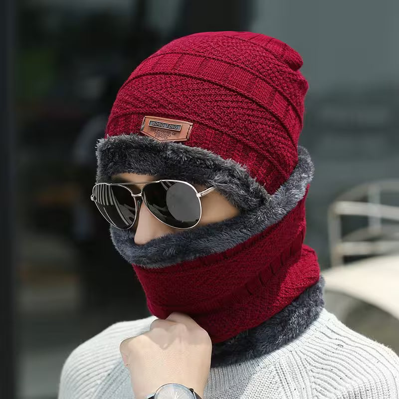Person wearing a red knitted beanie and gray scarf with sunglasses, against a blurred background.