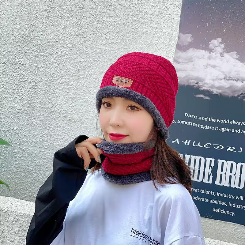 Person wearing a red and gray knit hat and scarf against a light-colored wall with a poster.