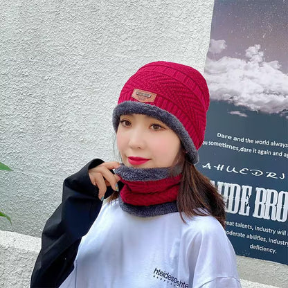 Person wearing a red and gray knit hat and scarf against a light-colored wall with a poster.