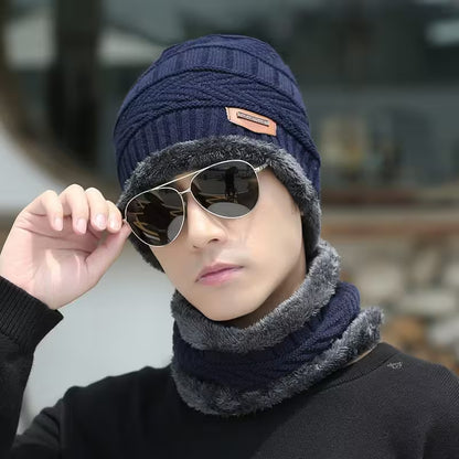 Person wearing a navy knit beanie and gray scarf with sunglasses, blurred background
