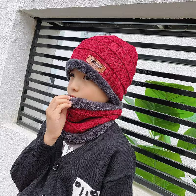 Child wearing a red and gray knit hat and scarf against a black metal gate.