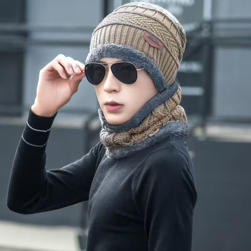 Person wearing a knitted hat and scarf with sunglasses, standing against a blurred background.
