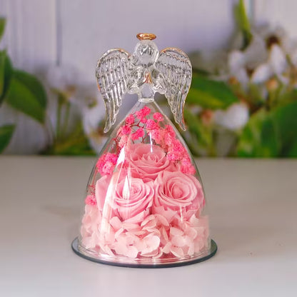 Decorative angel figurine with pink roses inside a glass dome on a white surface.