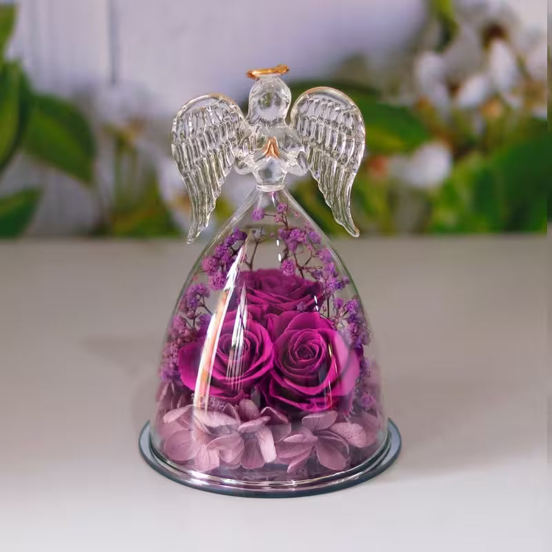Decorative angel figurine with pink roses under a glass dome on a white surface.