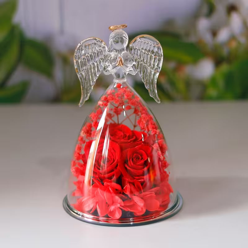 Decorative angel figurine with red roses inside a glass dome on a white surface.