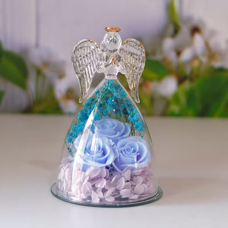 Decorative angel figurine with blue roses and crystals inside a glass dome on a white surface.