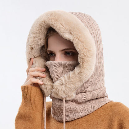 Person wearing a beige knitted balaclava with fur trim on a white background