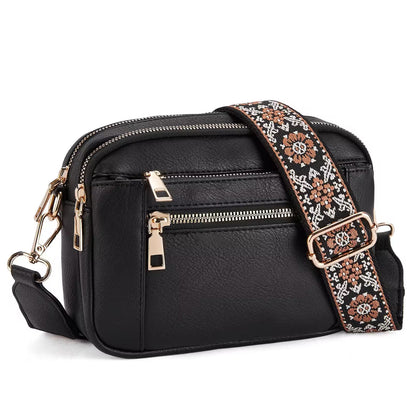 Black leather crossbody bag with a patterned strap on a white background