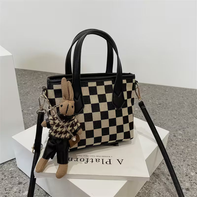 Black and white checkered handbag with a rabbit keychain on a white platform.