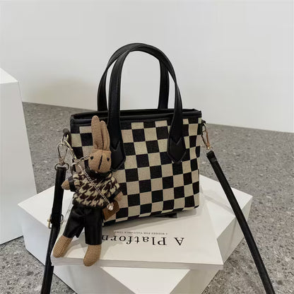 Black and white checkered handbag with a rabbit keychain on a white platform.