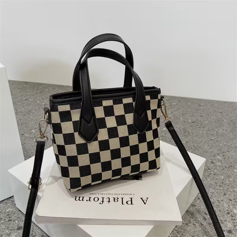 Checkered handbag with black handles on a white platform