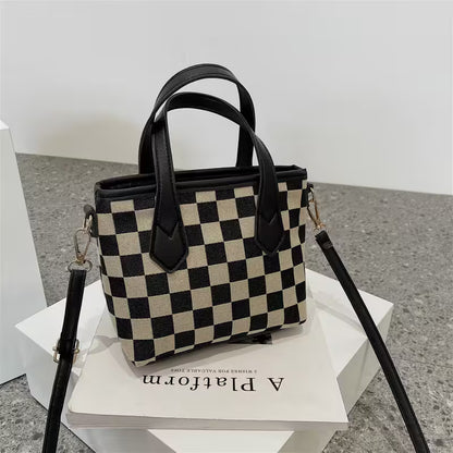 Checkered handbag with black handles on a white platform
