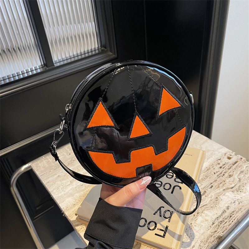 Round black handbag with orange jack-o'-lantern face design held by a person.