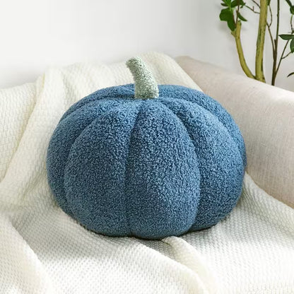 Blue pumpkin-shaped pillow on a white surface with a plant in the background