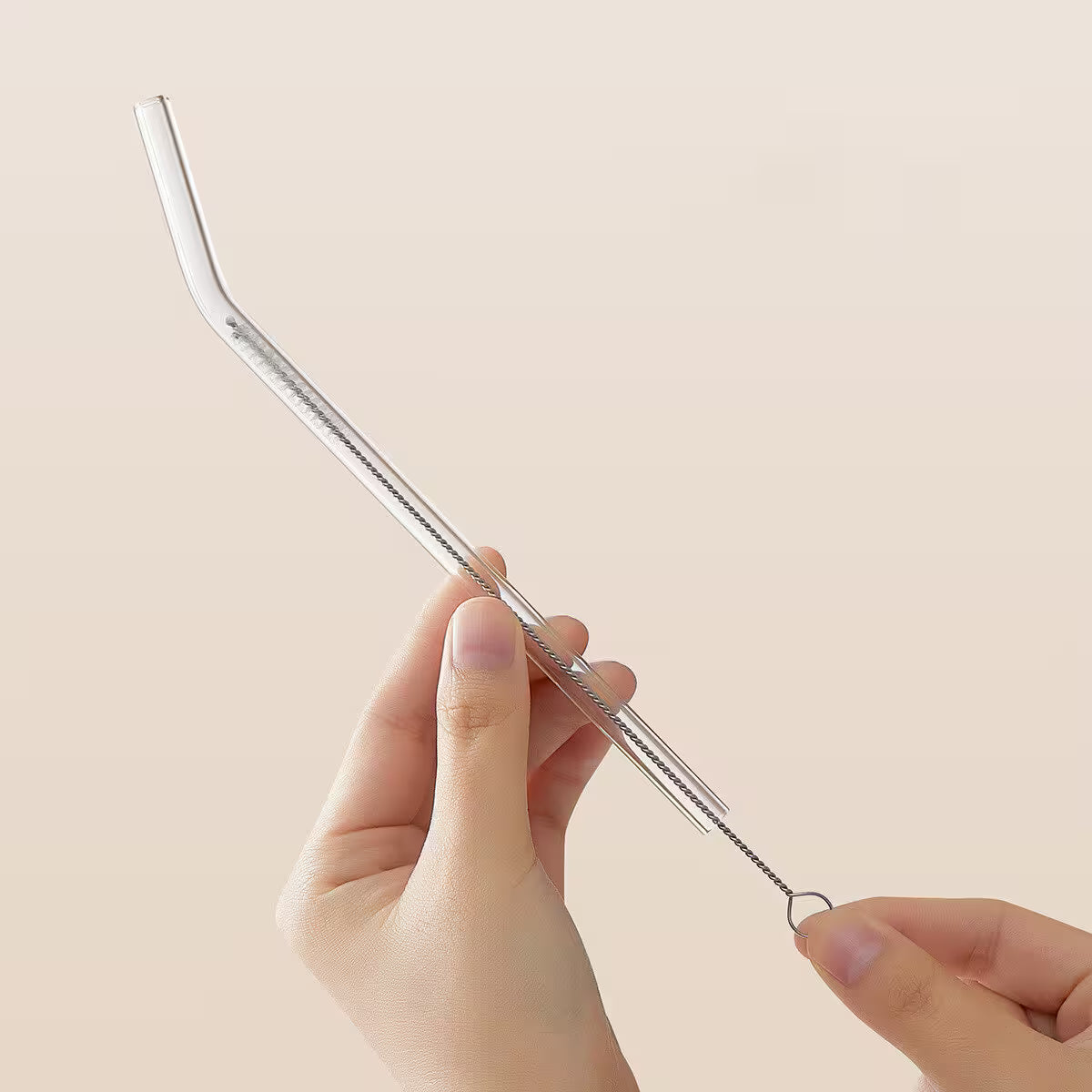 Clear metal straw held by a hand against a beige background