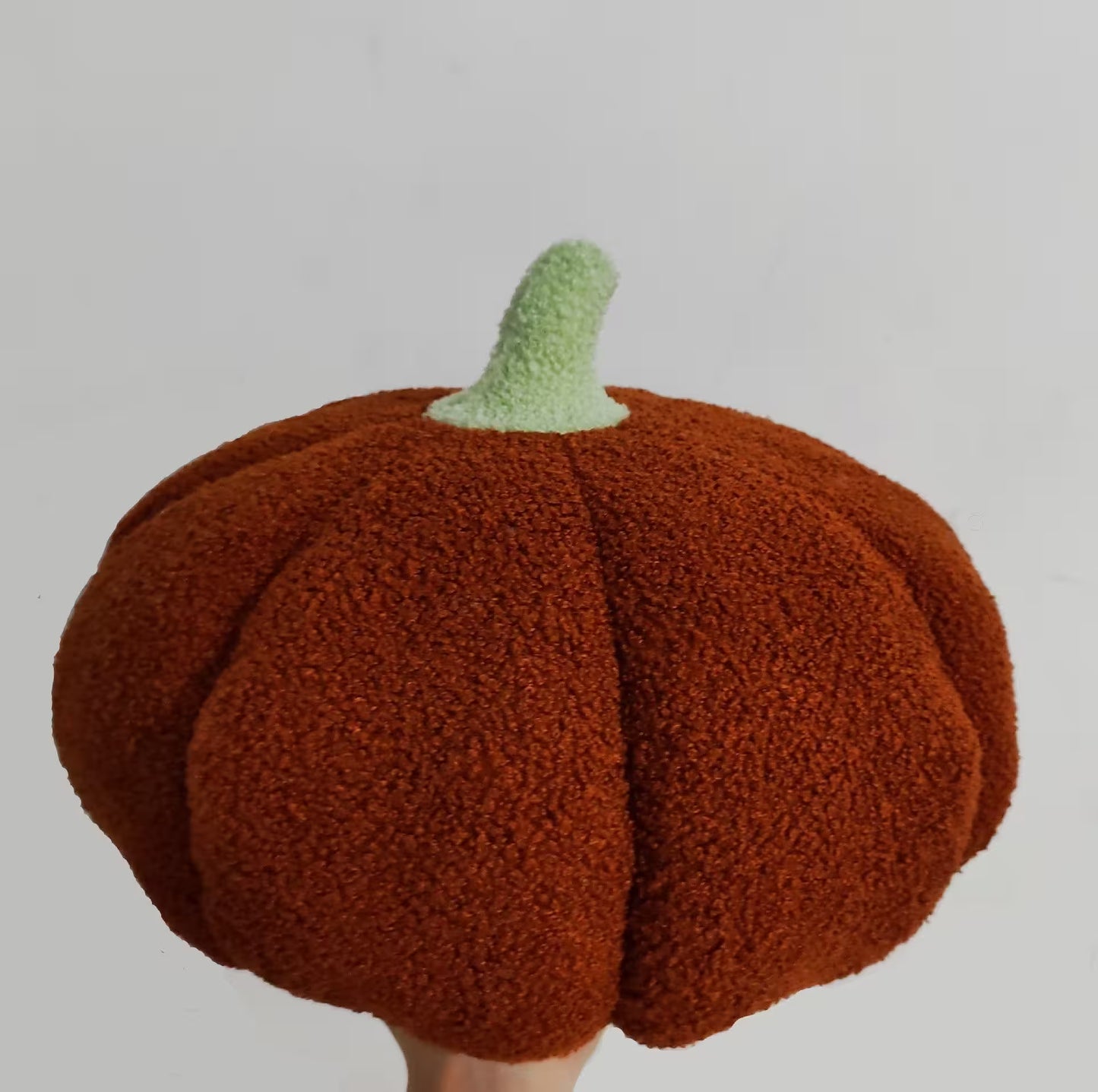 Knitted pumpkin hat with a green stem on a light gray background