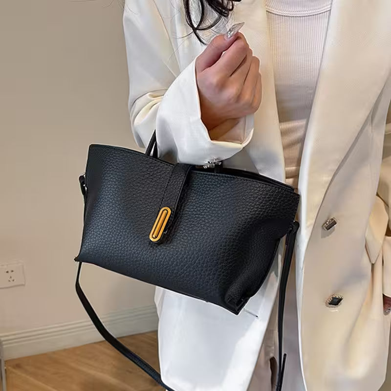 Person holding a black handbag with a yellow accent in a neutral setting
