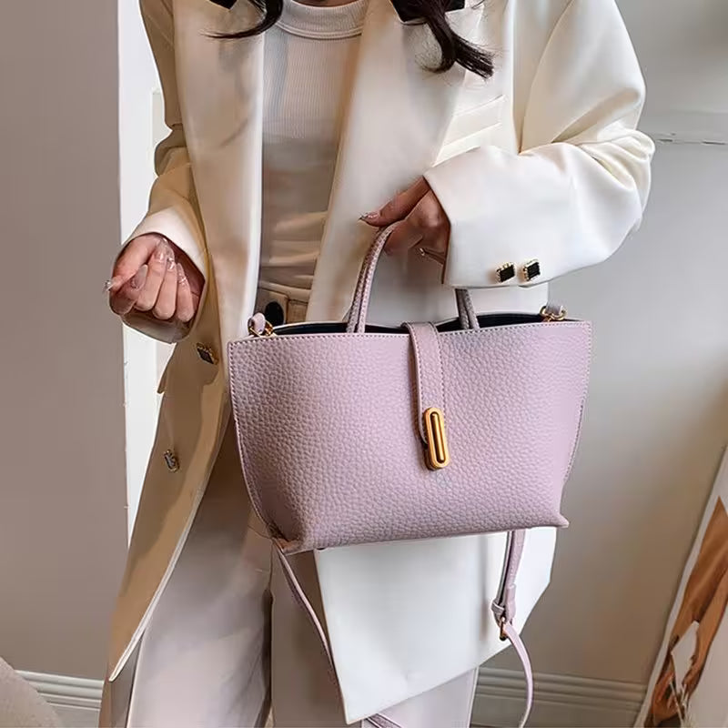 Person holding a light purple handbag with a gold clasp against a neutral background