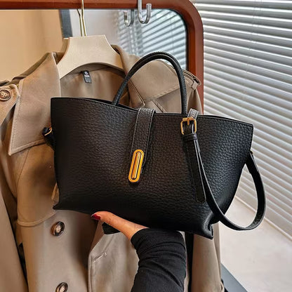 Black handbag with gold accent held by a person against a beige trench coat.