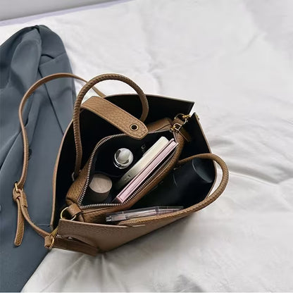 Brown leather handbag with makeup items on a white surface