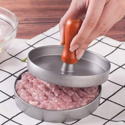 Hand using a meat grinder to process ground meat on a checkered tablecloth.