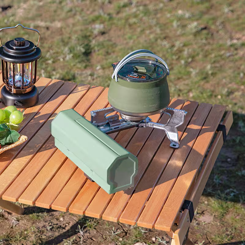 Camping stove with kettle and lantern on a wooden table outdoors
