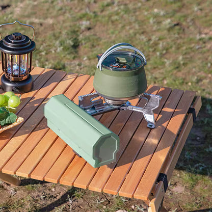 Camping stove with kettle and lantern on a wooden table outdoors