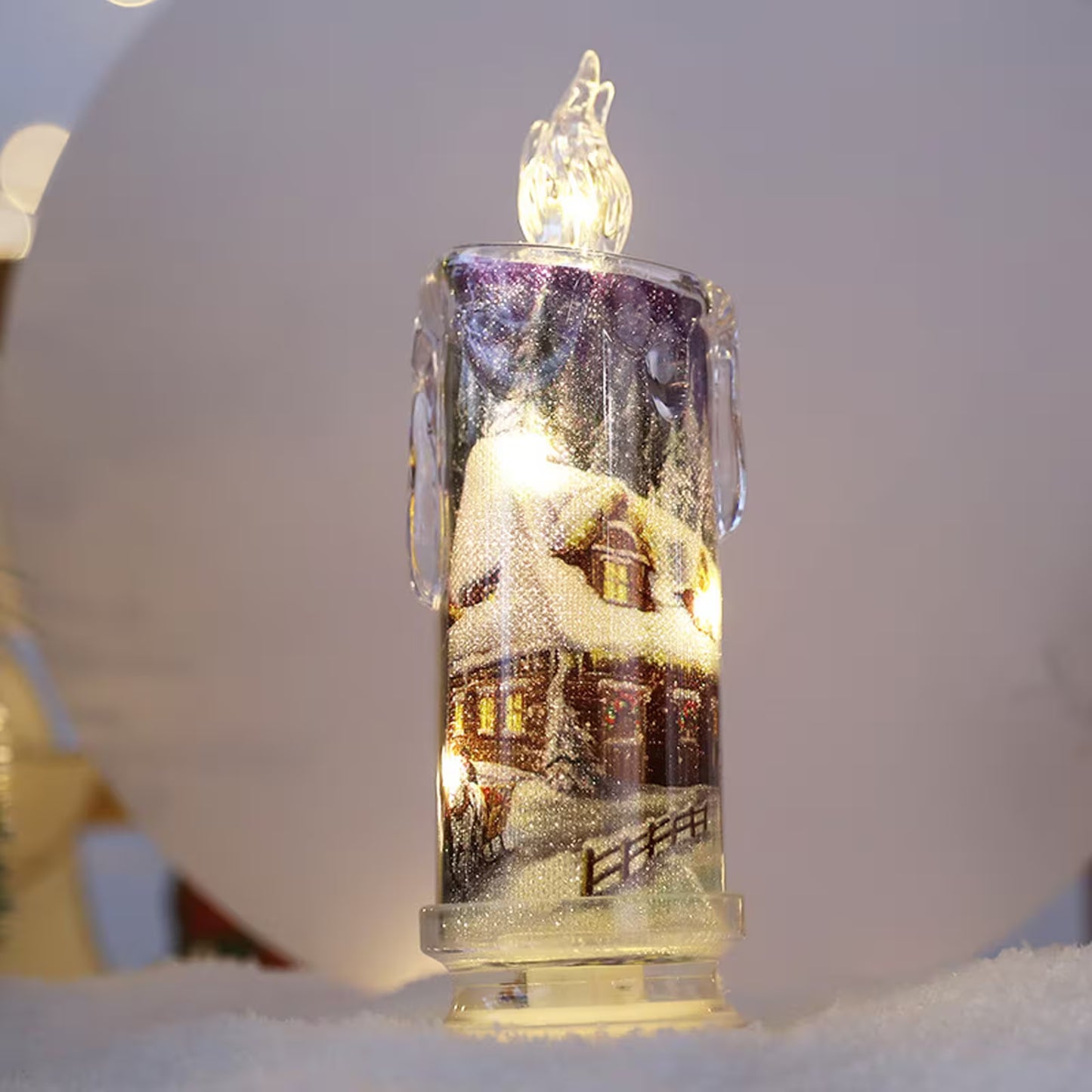 Decorative candle-shaped light with a snowy village scene inside, on a white background.